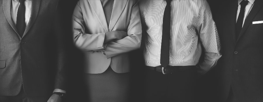 Cuerpo desde final de cuello a rodillas de cuatro empresarios trajeados en color blanco y negro